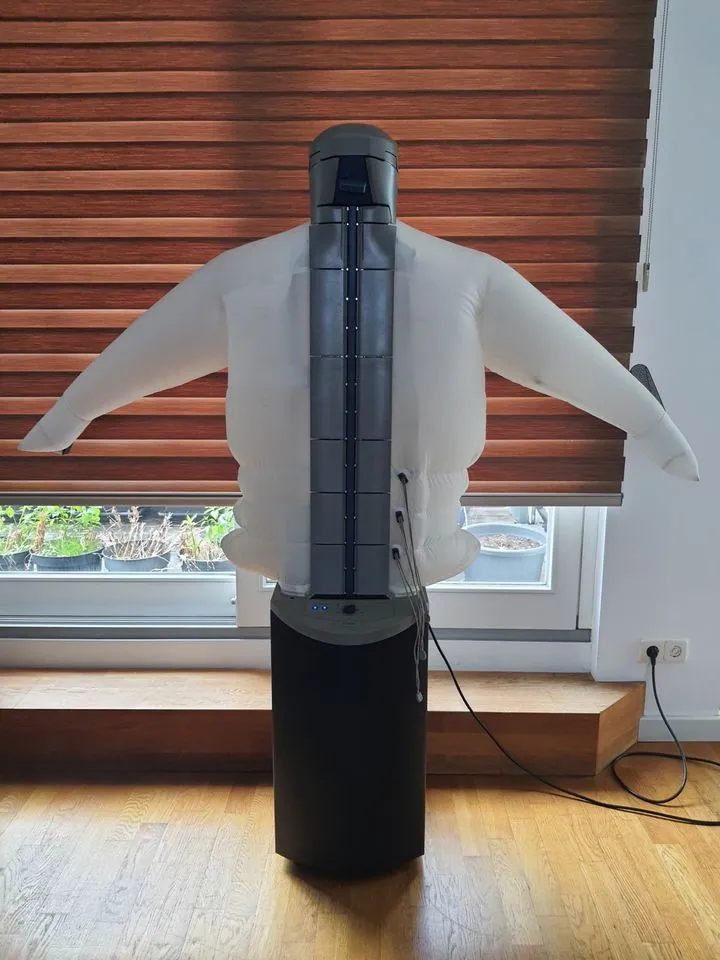Front view of an uncovered dressman with a translucent torso, outstretched sleeves and a dark base beside a window.