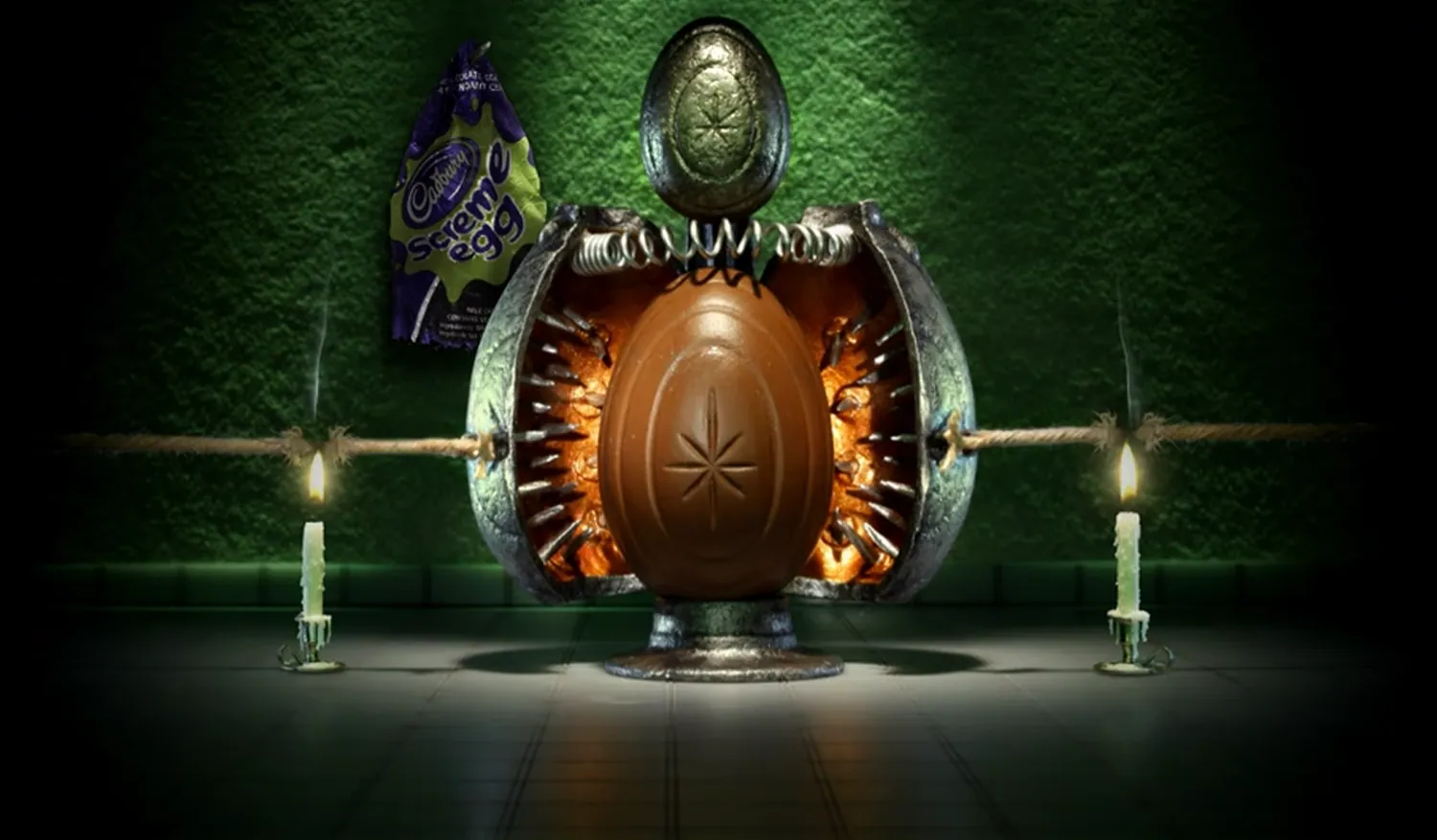 A Cadbury Screme Egg strapped inside a metal device between two candles, with green light behind it and a purple Screme Egg wrapper at upper left.