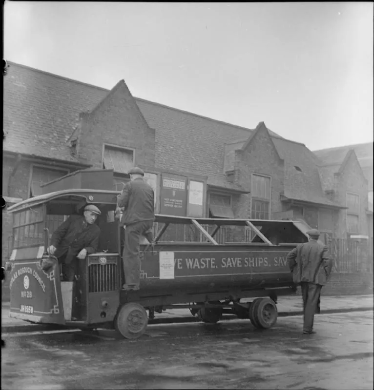 Three men stand on or beside a salvage lorry outside a brick building.