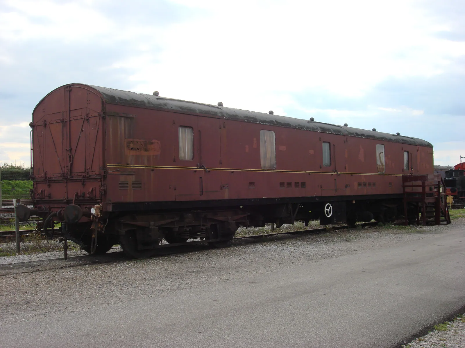 A preserved maroon railway van with large end doors and small windows stands outdoors beside railway tracks.