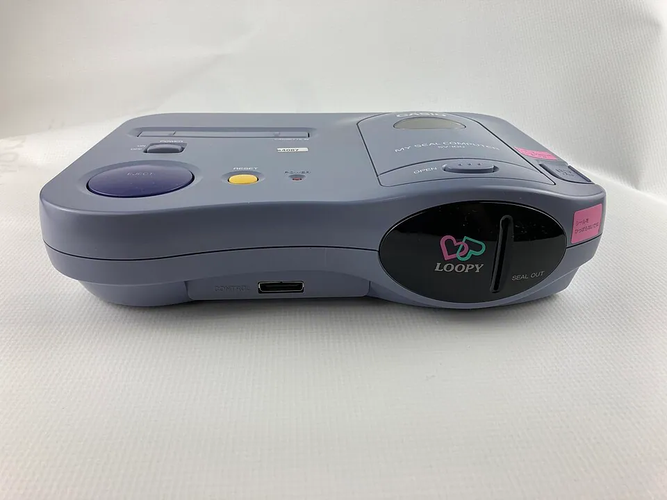 Front three-quarter view of a grey and purple Casio Loopy console against a white background.