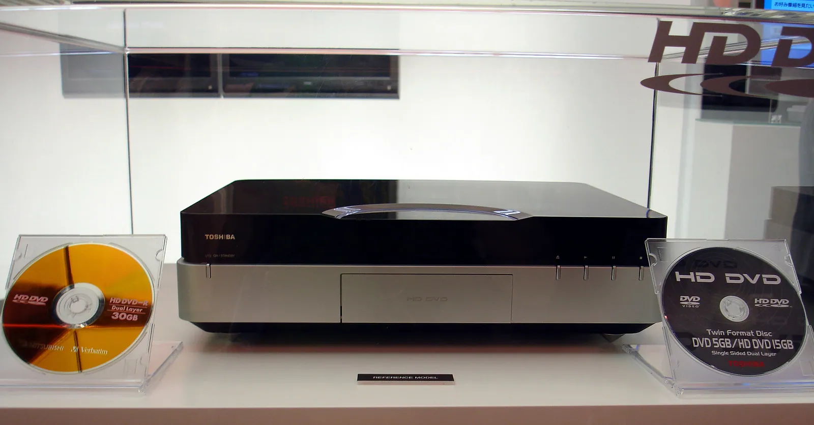 Toshiba HD DVD player displayed between an orange HD DVD-R disc and a black dual-format DVD and HD DVD disc.