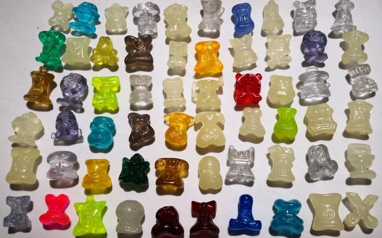 Rows of small translucent plastic collectible figures in red, green, yellow, blue, brown and clear, arranged against a white background.