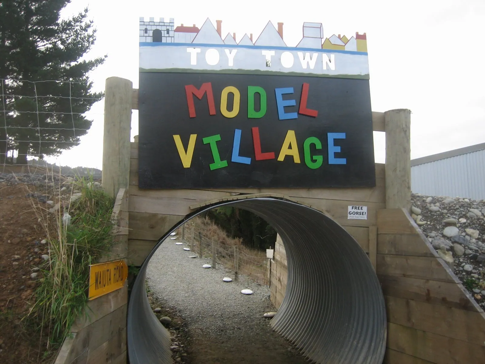 Entrance to Little Earth Model Village in New Zealand, featuring a colourful “Toy Town Model Village” sign above a corrugated tunnel walkway.