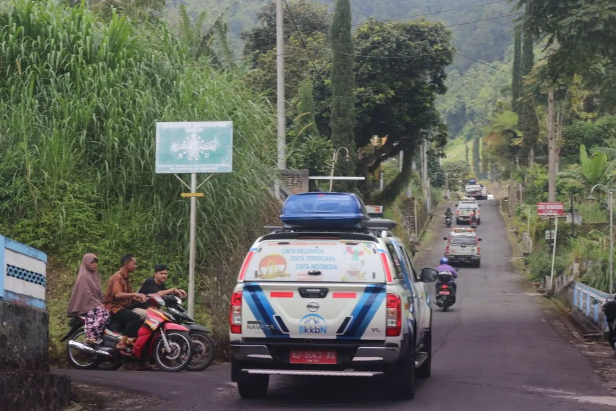 Convoy of modern blue-and-white BKKBN Mobil Unit Penerangan vehicles travelling through a green hilly landscape in Karanganyar in 2023.
