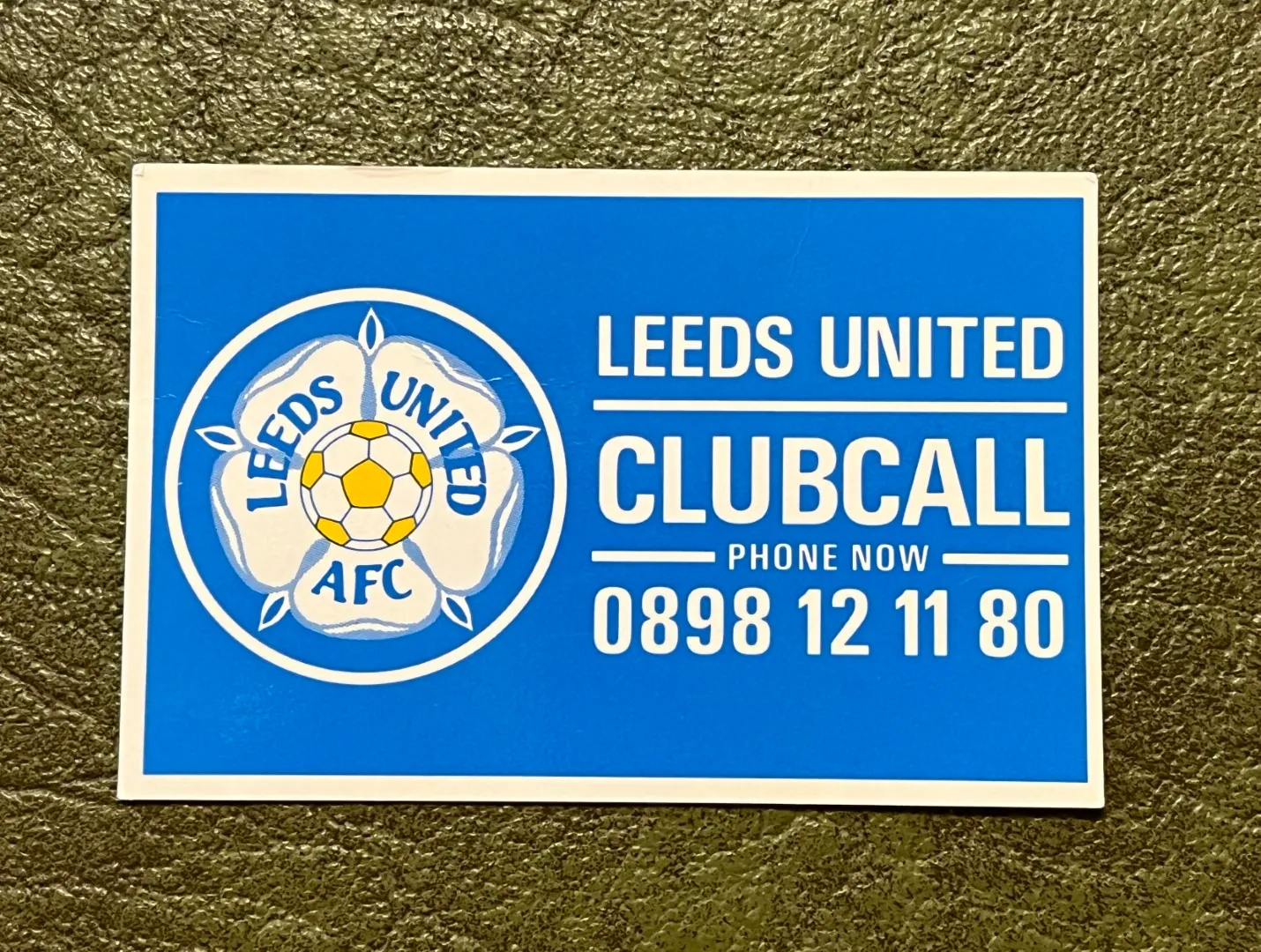Blue-and-white Leeds United Clubcall card on a textured dark surface, with the club crest and large text reading “LEEDS UNITED CLUBCALL — PHONE NOW — 0898 12 11 80.”