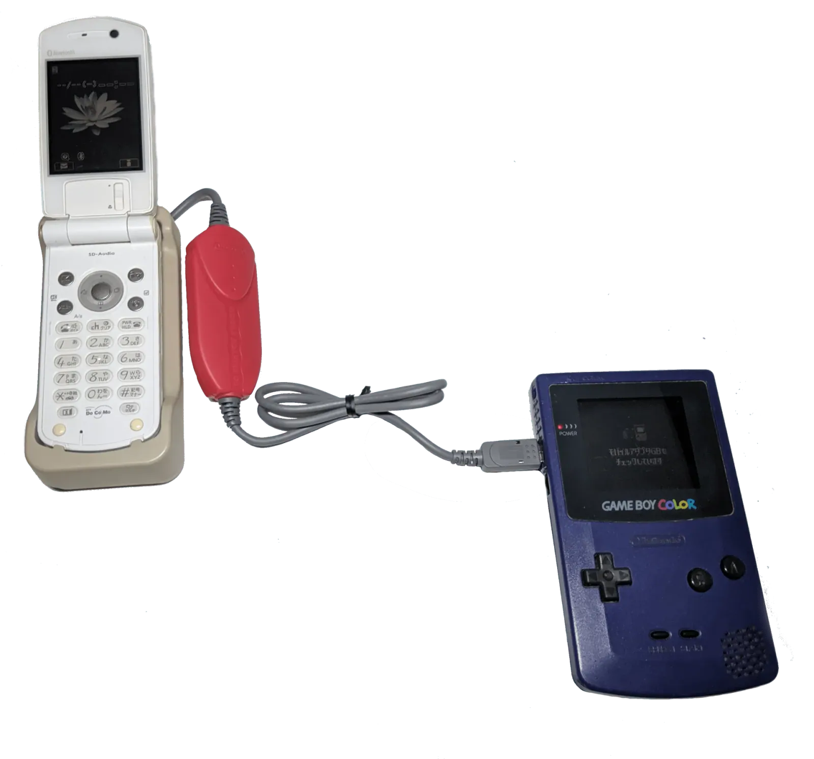 A blue Mobile Adapter GB linking a translucent Game Boy Color to a Japanese mobile phone beside a Pokémon Crystal cartridge.