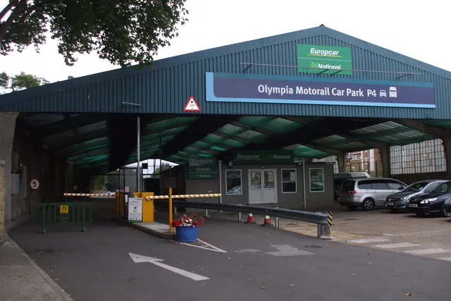 An entrance canopy reads Olympia Motorail Car Park P4 above parked cars and car-rental signs.