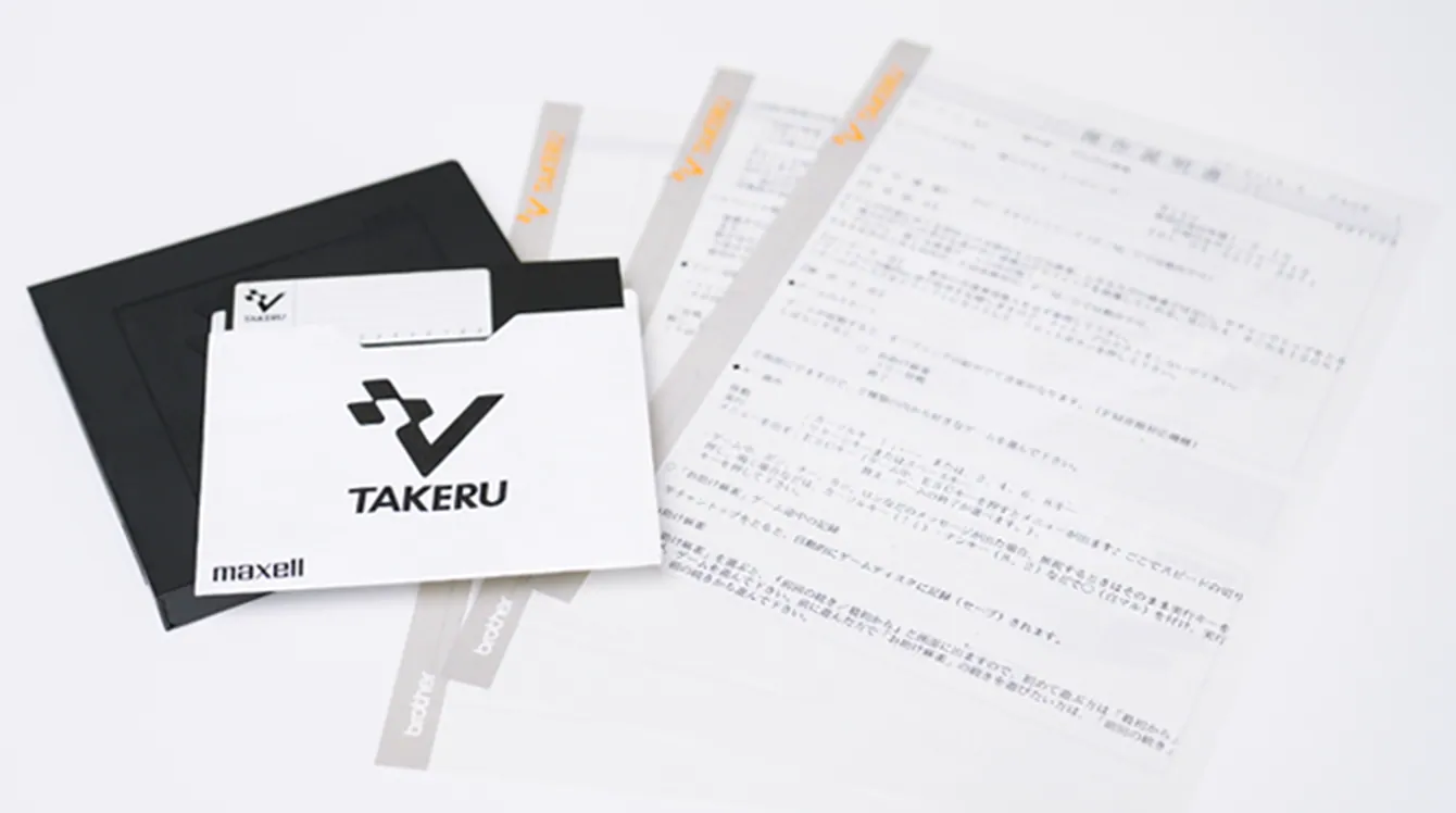 Black floppy disk, white TAKERU-branded protective sleeve and several Japanese instruction sheets arranged on a white background.