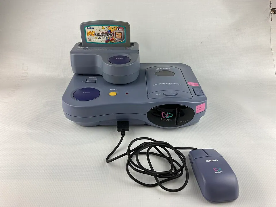 Casio Loopy console connected to its purple mouse, with the Magical Shop expansion and a game cartridge fitted.