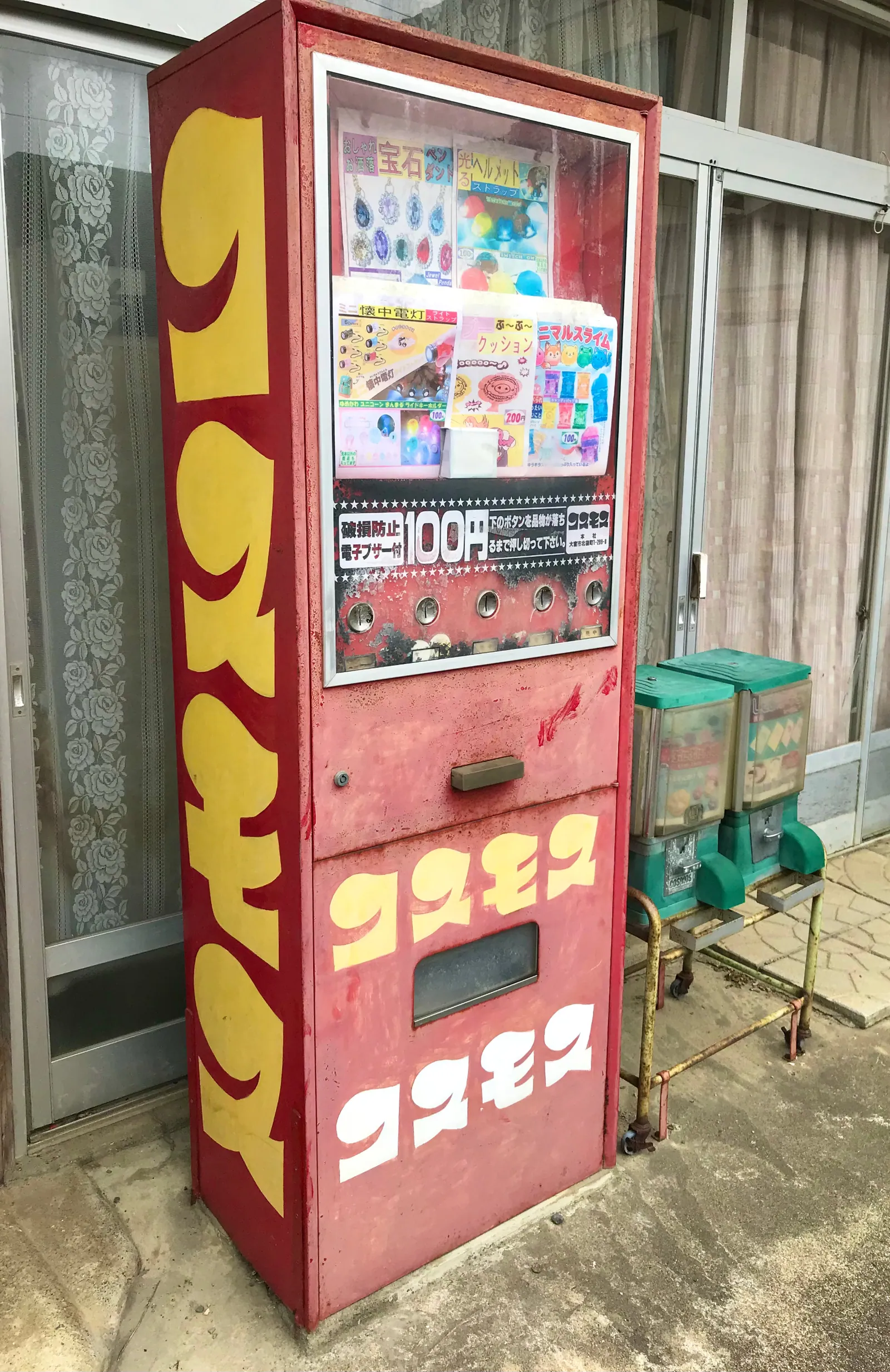 Full-height oblique view of a weathered red vending cabinet outside a building.