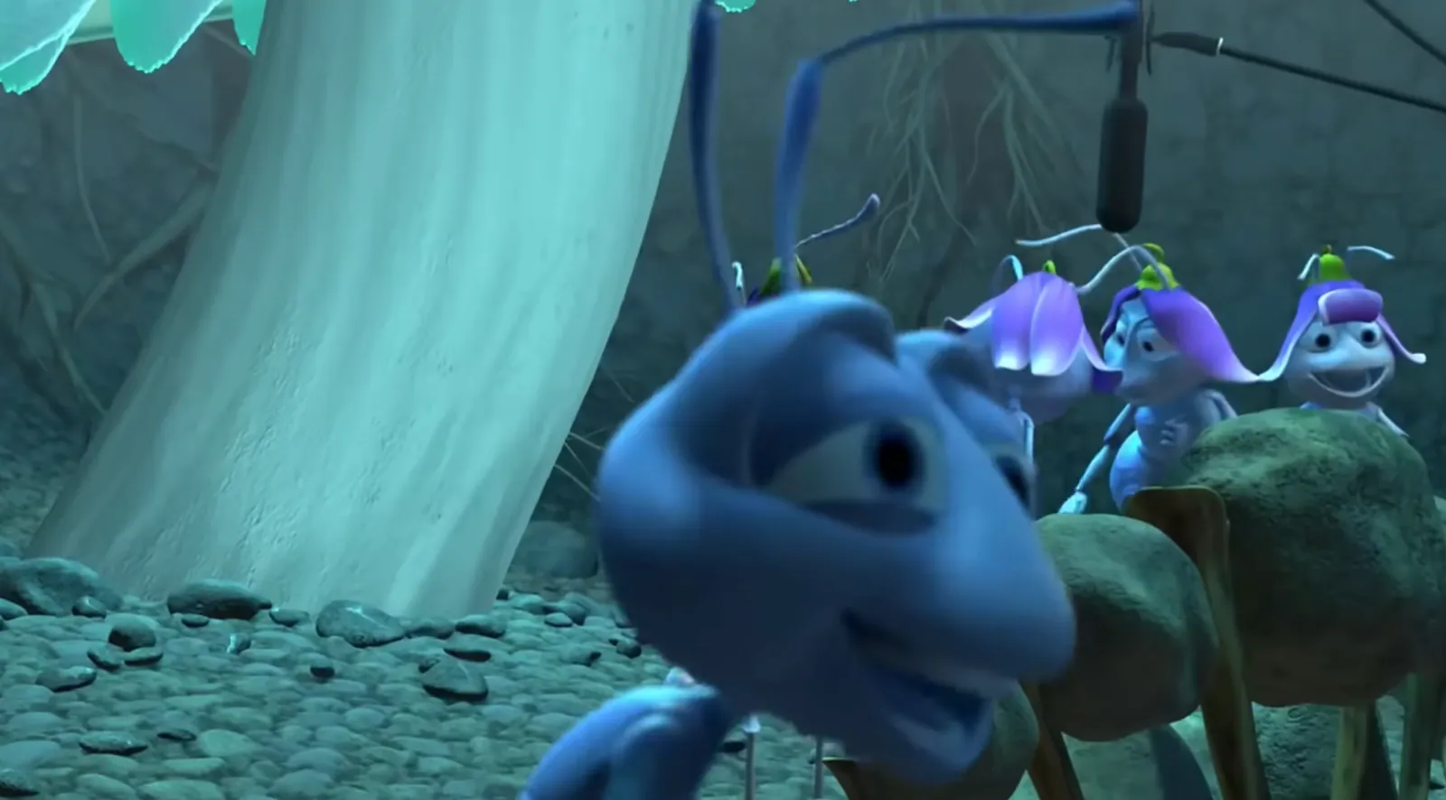 A computer-animated blue ant appears out of focus close to the camera while three other ants wearing purple flower petals stand behind it; a black boom microphone hangs visibly above them.