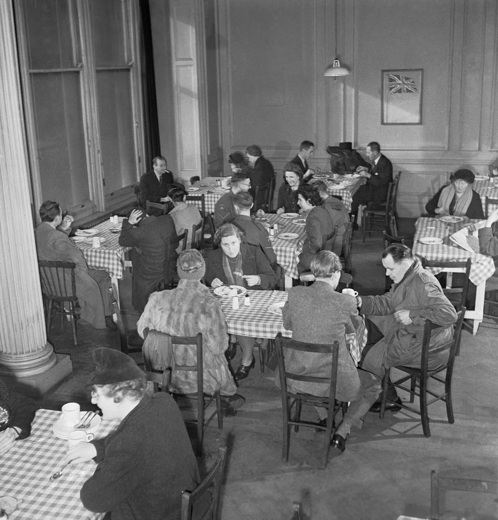 Diners sit at closely packed tables with checked cloths in a large dining room.