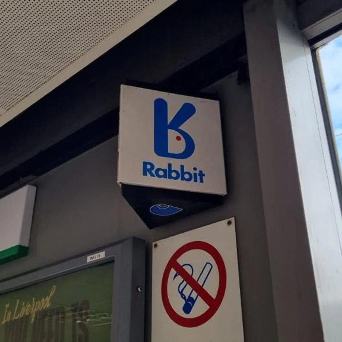 Photograph of a square Rabbit sign with a blue stylized rabbit logo and the word “Rabbit,” mounted indoors above a sign showing a crossed-out telephone handset symbol.